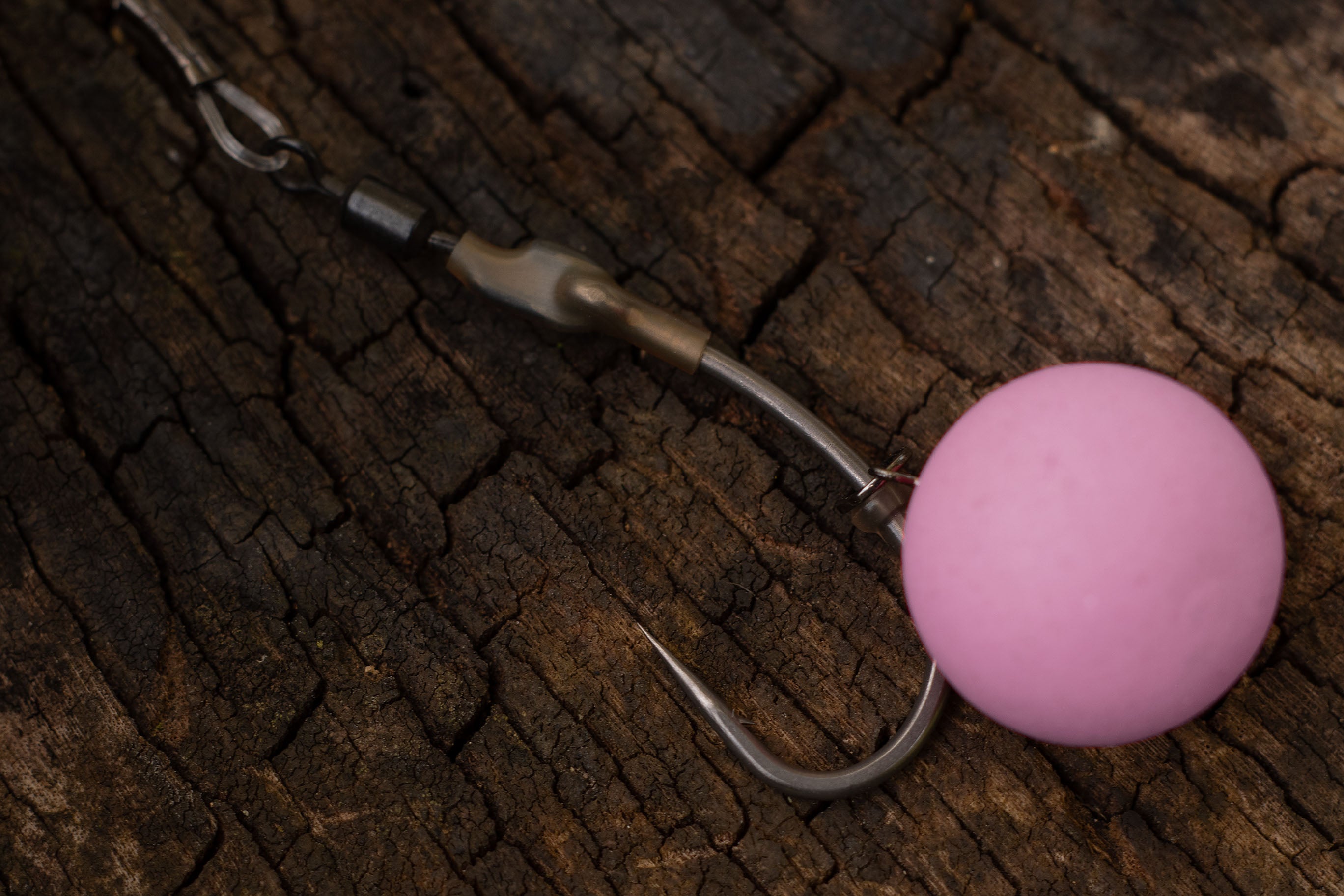 A spinner rig made with a size 4 Curve shank hook with a washed out pink pop up boilie attached to a micro hook ring swivel sits on a weathered stump.
